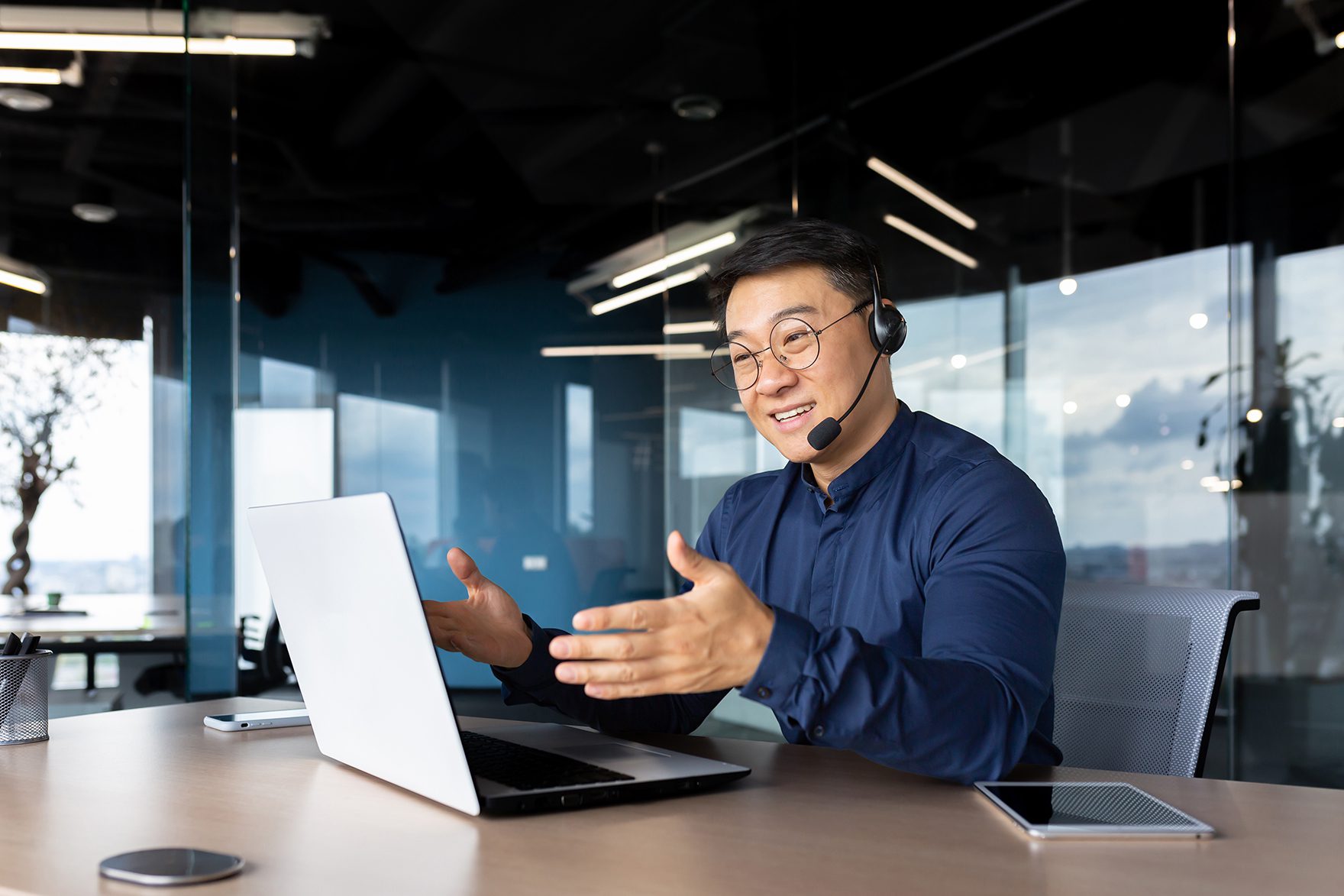 Asian With A Headset Is Talking On Video Call, Man Inside Office Smiling And Gesturing Joyfully In An Online Meeting, A Businessman Is Telling His Colleagues, A Customer Service Tech Support Worker